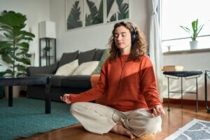 Young mindful woman wearing headphones listening music doing meditation at home.
