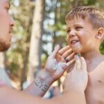Father apply sunscreen on child face for protection or safety while camping in a forest or woods for vacation or holiday. Lotion, cream and dad care for kid with skincare product in outdoor adventure. how to choose sunscreen