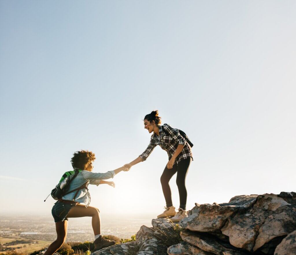 a woman helping another woman up on a hiking trail
