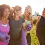 four middle-aged women walking together while holding yoga mats on a warm sunny day
