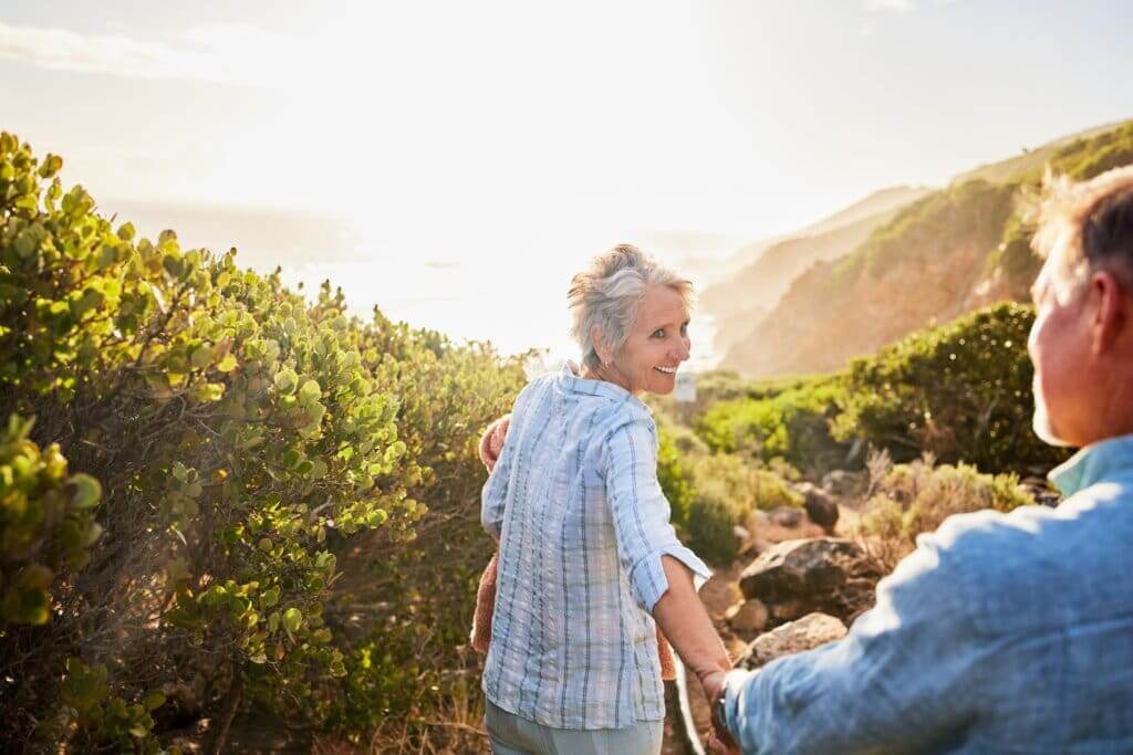 gracefully aging woman smiling back at her partner as they walk down a trail along a coastal cliff