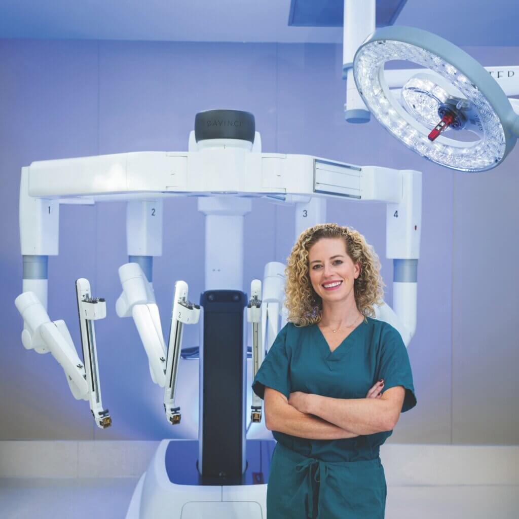 surgeon and gastroenterologist Dr. Alexandra Kovar standing in front of surgical machinery while wearing dark teal scrubs