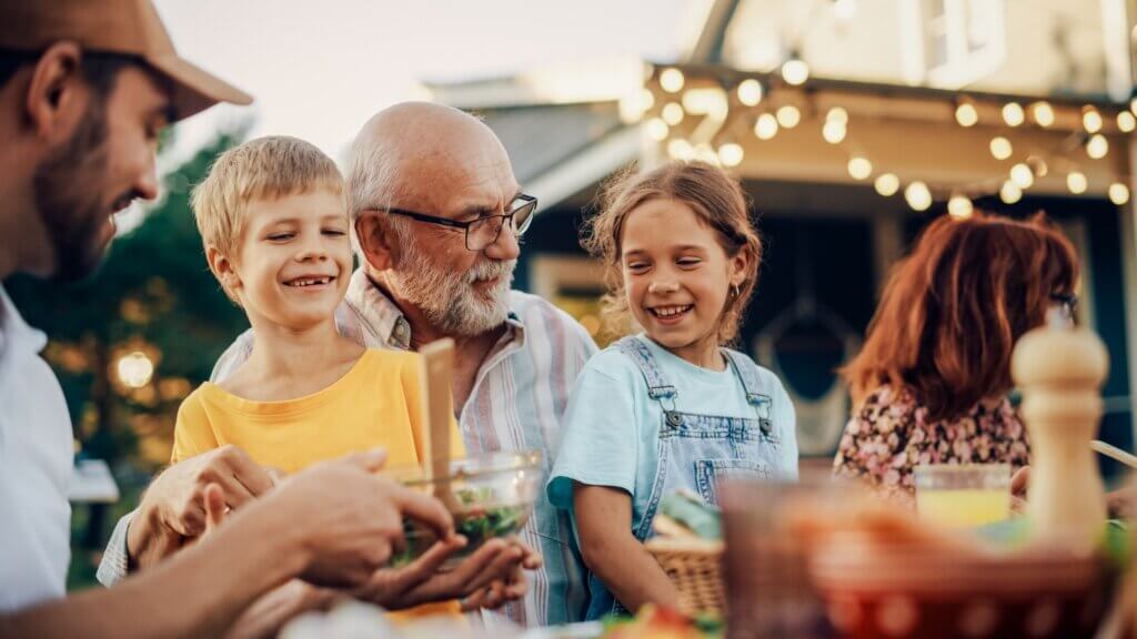 retired grandfather at his senior living community sitting at a table with his two smiling grandchildren on his lap