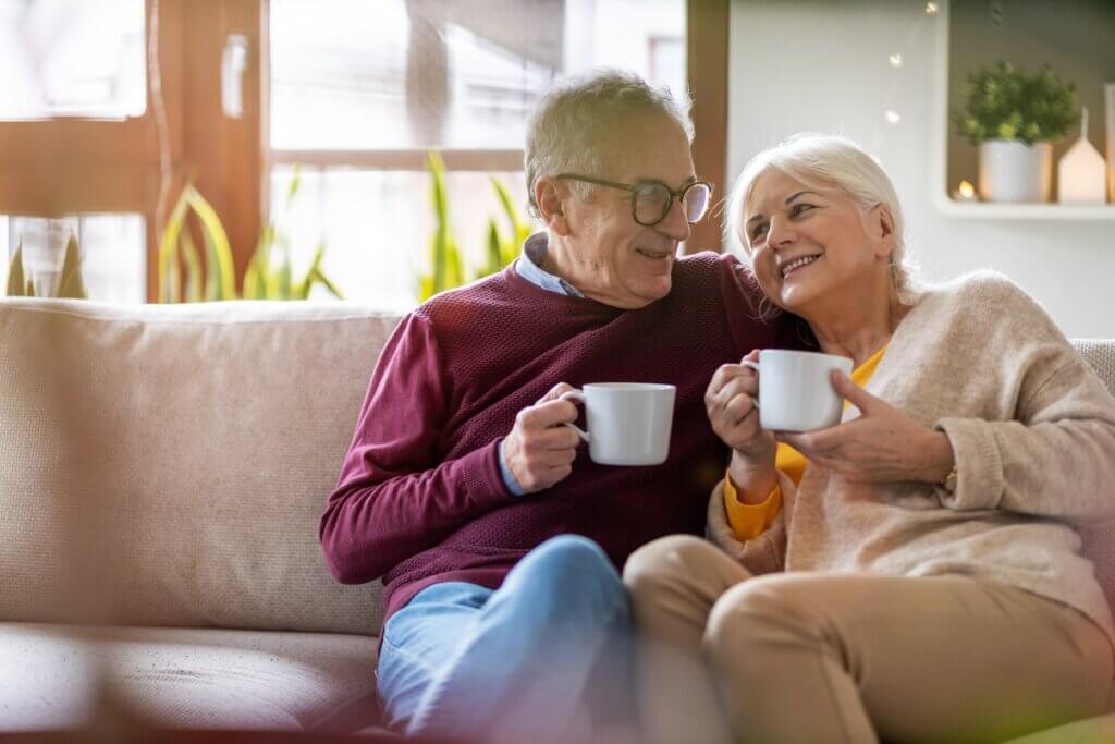 senior couple sitting on the couch of their independent living residence and drinking coffee together after evaluating what to look for in a retirement community