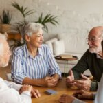 group of four seniors who have chosen the right senior living community for them sitting at a table playing cards and smiling at each other
