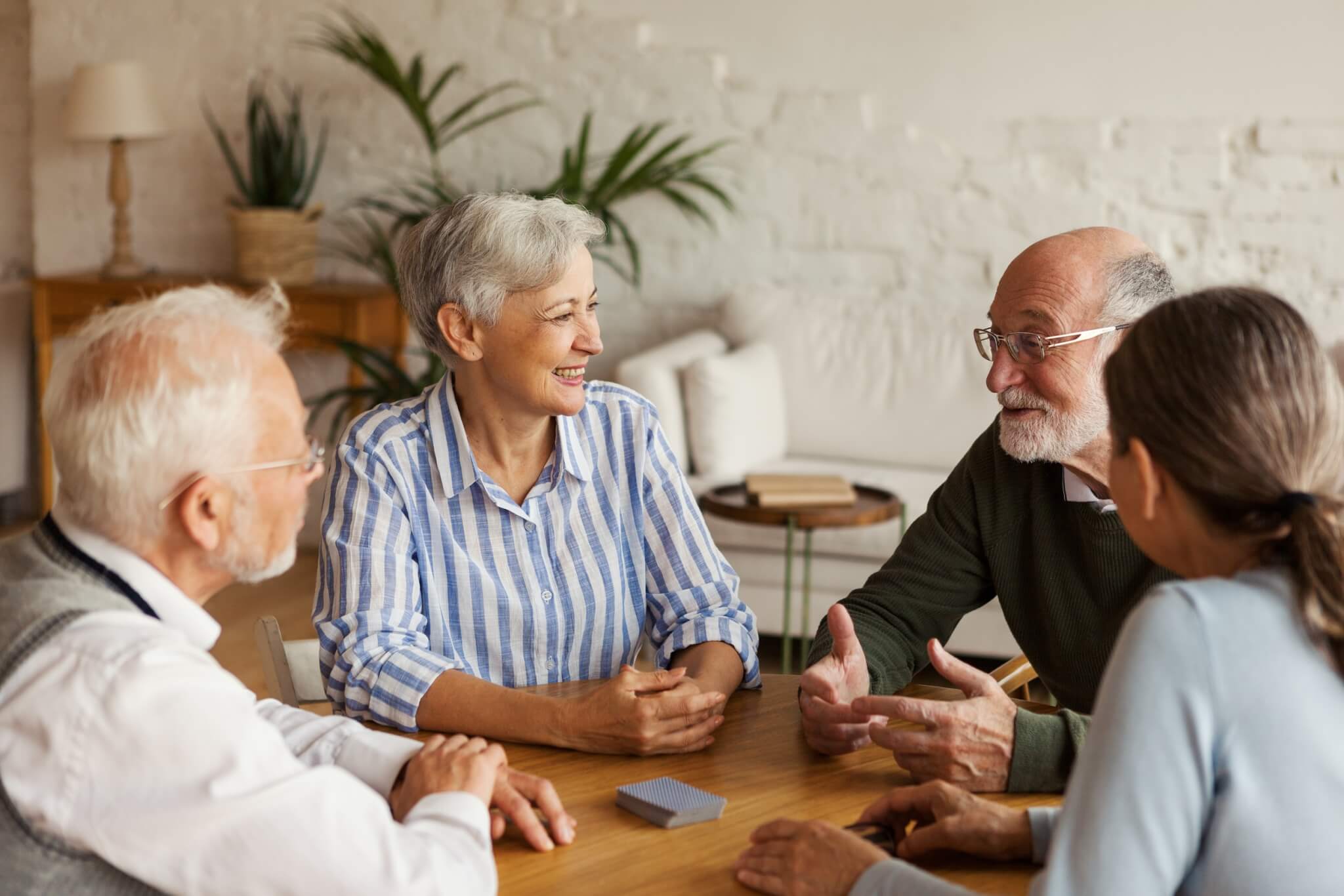 group of four seniors who have chosen the right senior living community for them sitting at a table playing cards and smiling at each other