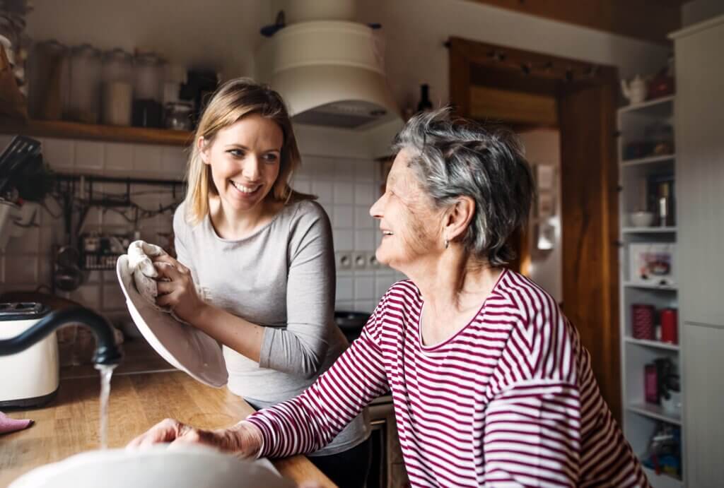 at home dementia caregiver helping an elderly woman wash her dishes