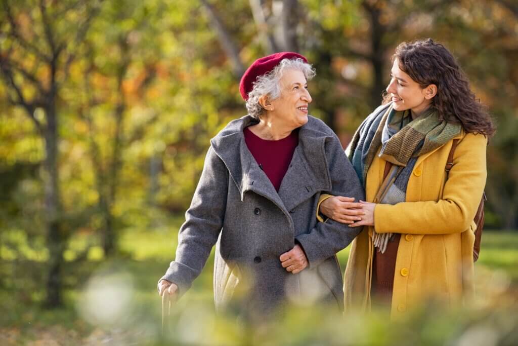 a caregiver in a yellow coat showing how to help someone with dementia by taking them on a guided walk outside
