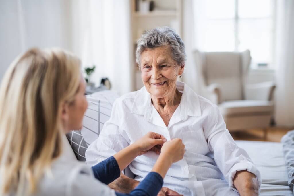 a caregiver buttoning an elderly woman's blouse showing how to help someone with dementia who is still living at home