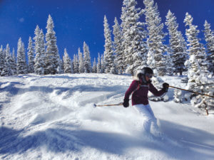 person skiing down a hill with snow-covered trees behind them