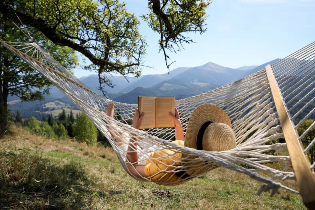 woman swinging in a hammock while reading a book during her technology free digital detox vacation retreat in the mountains