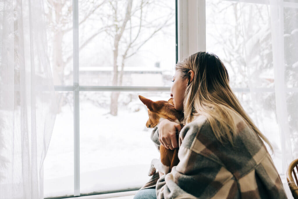 woman with the winter blues sitting by a window with her dog so she can use light therapy to address her symptoms of seasonal depression
