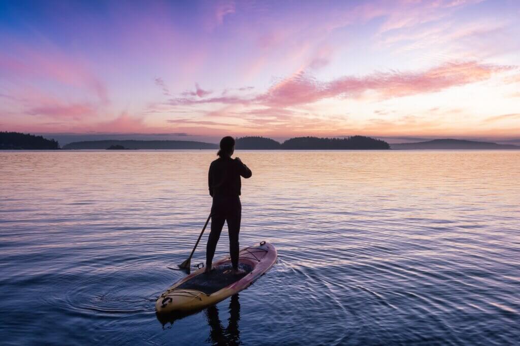 person stand up paddleboarding on a lake during blue hour with purple skies above