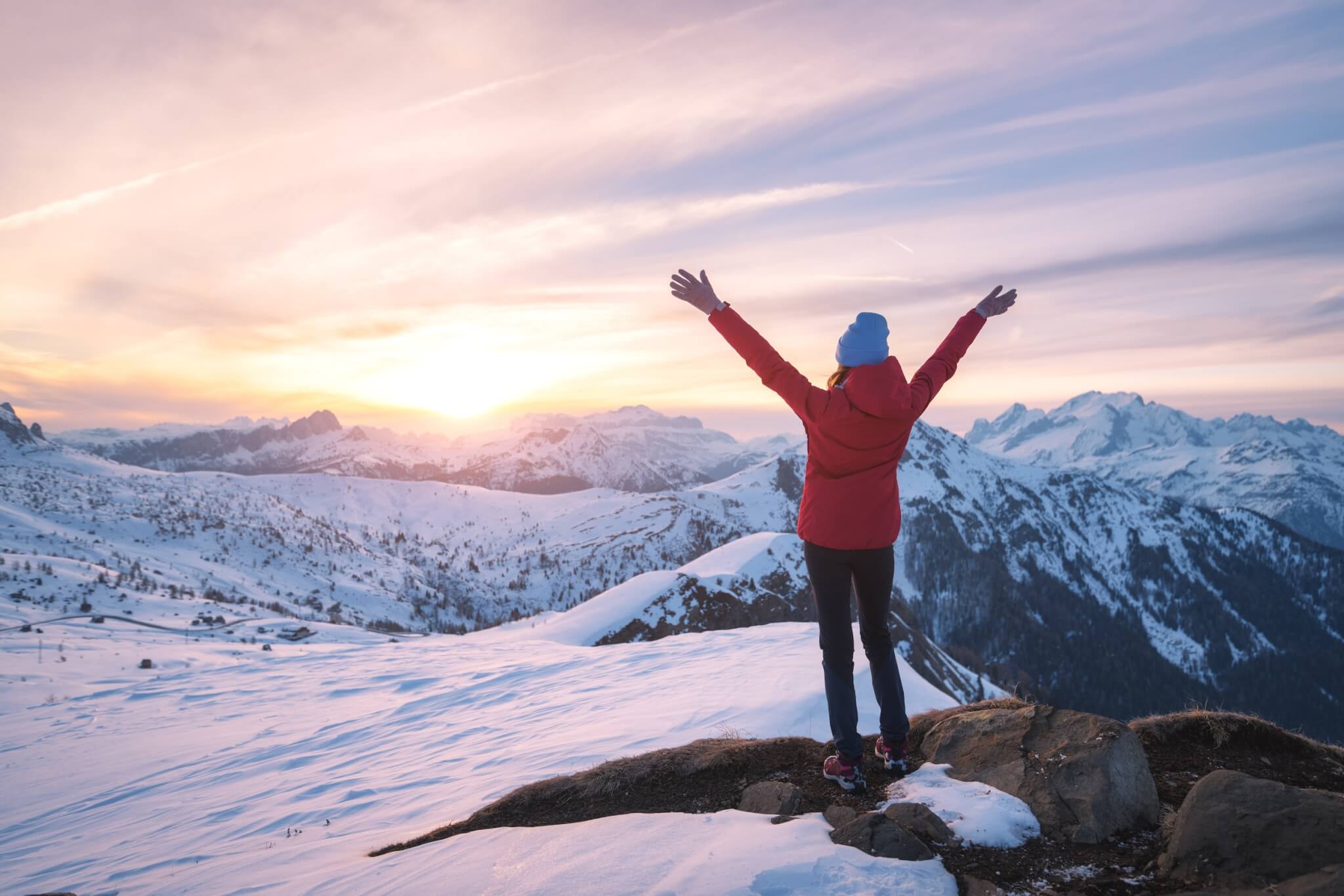 woman who does light therapy in the winter to deal with her anxiety and depression standing at the top of a snowy mountain peak looking out at the sunrise