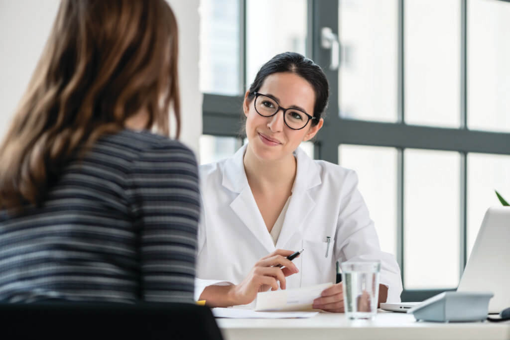 doctor wearing glasses siting at a table smiling at a patient
