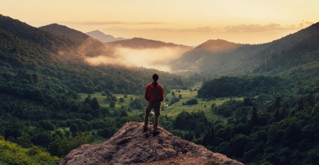 man standing on the edge of a cliff staring out at the mountains
