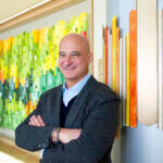 image of Dr Richard Becker standing in the lobby of Aspen Valley Hospital smiling at the camera with his arms crossed over his chest