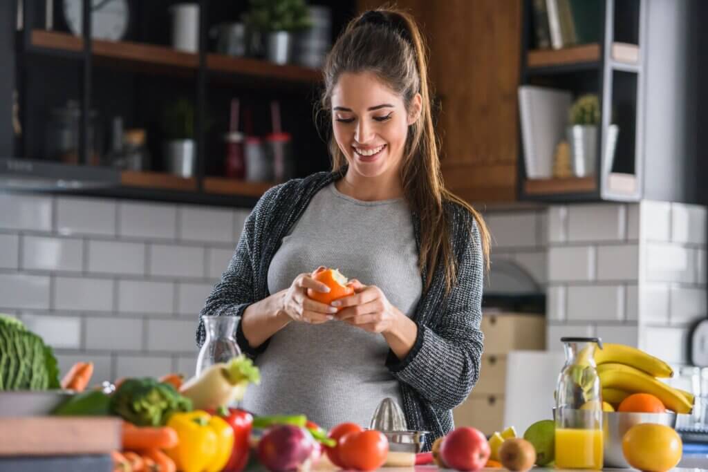 pregnant woman smiling while peeling an orange in her kitchen