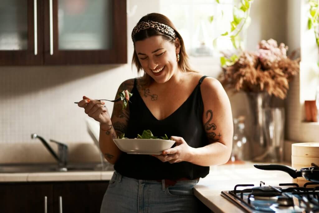 woman smiling as she holds a forkful of salad