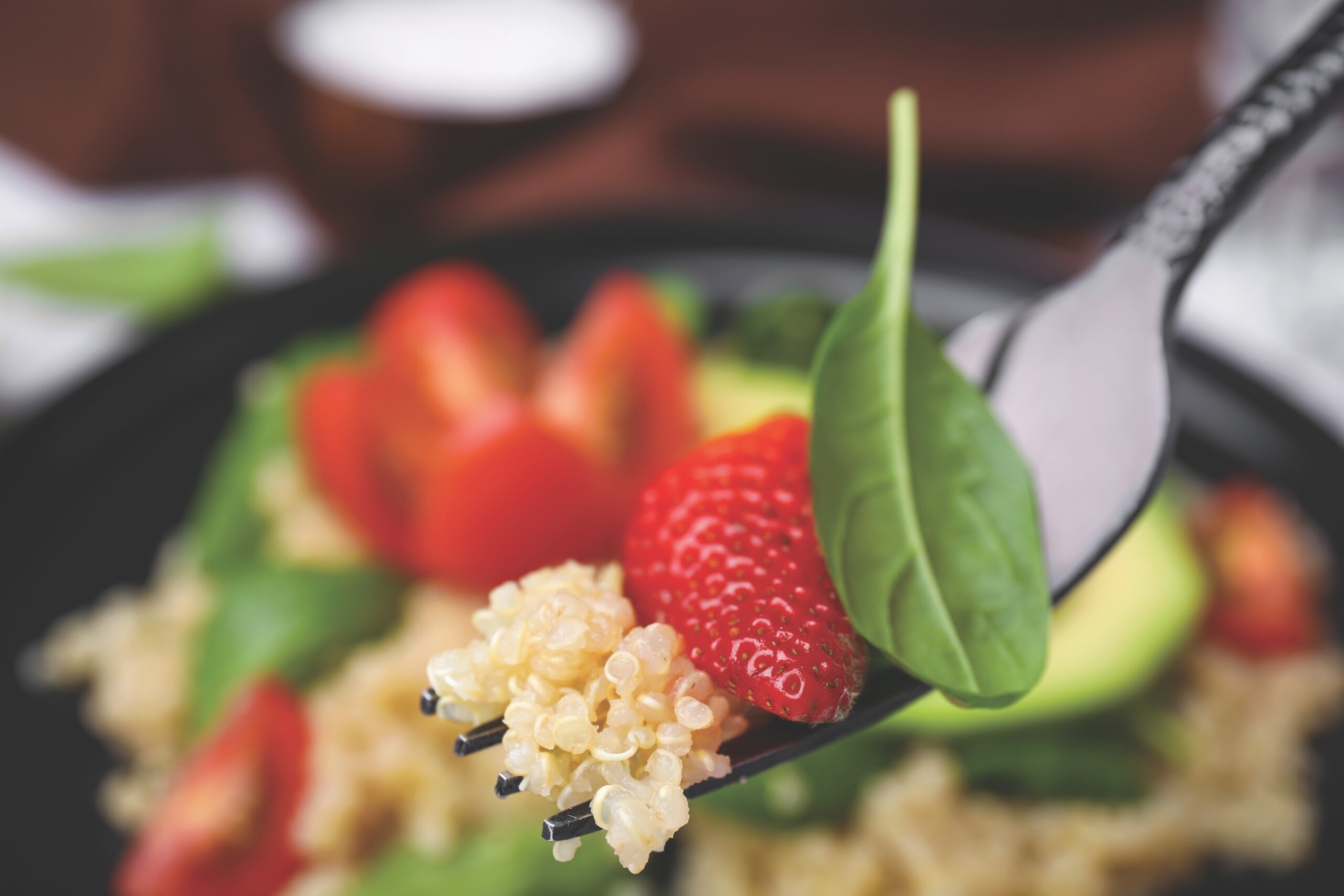 fork holding quinoa along with a strawberry and a leaf of spinach